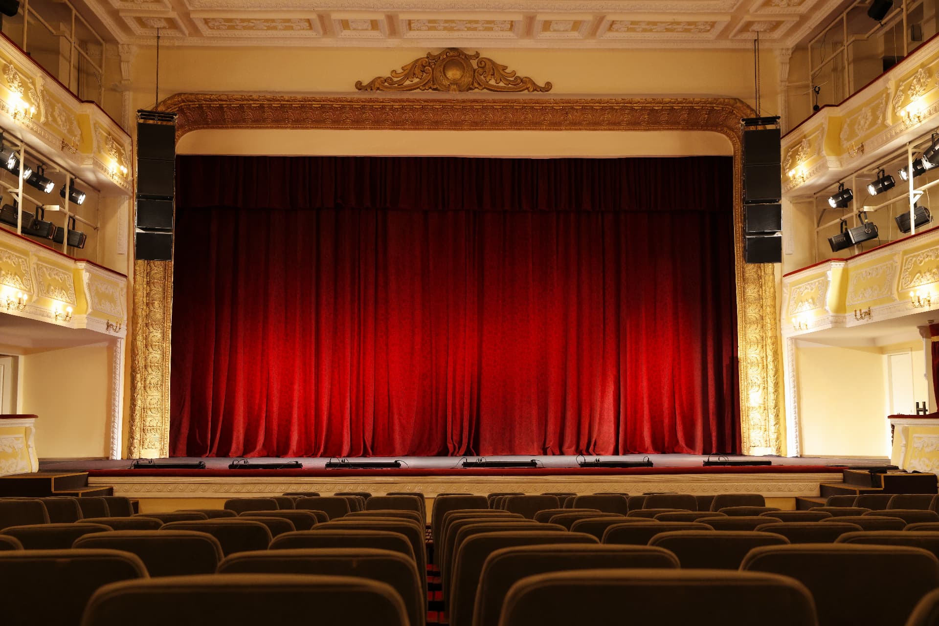 An elegant theatre auditorium with red curtains and gold balconies