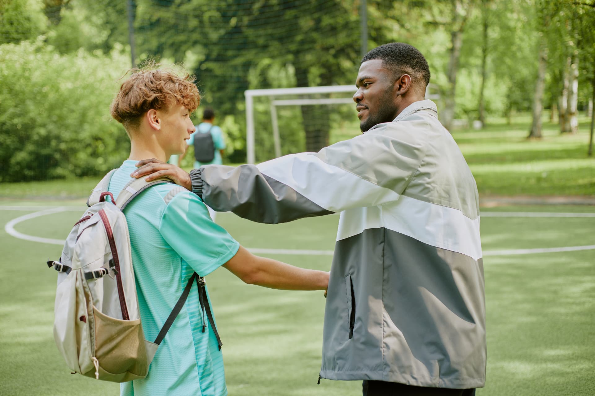 A mentor with his hand on a young person's shoulder on a sports pitch